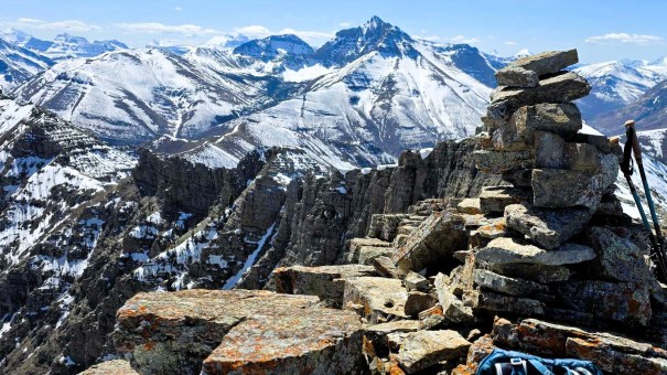 Summit cairn overlooking snow-covered mountains and valleys in the distance.