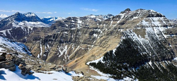 A panoramic view of rugged mountain peaks with snow patches and rocky terrain under a clear blue sky.