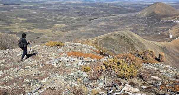 A hiker navigating rocky terrain on a mountain ridge with a vast landscape of rolling hills and valleys in the background.