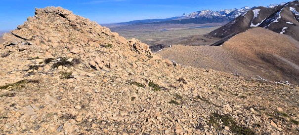 Rocky terrain at the summit of Dungarvan SE2, with panoramic views of the valley and snow-capped mountains in the distance.