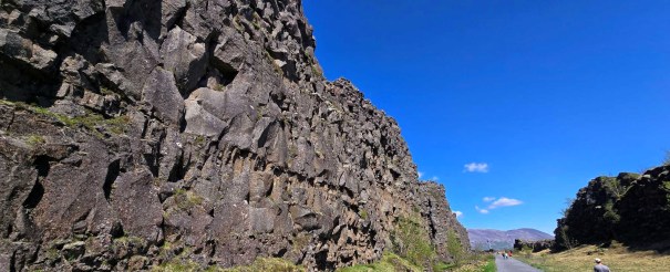 A scenic view of a basalt rock formation along a path in Þingvellir National Park, set against a clear blue sky.