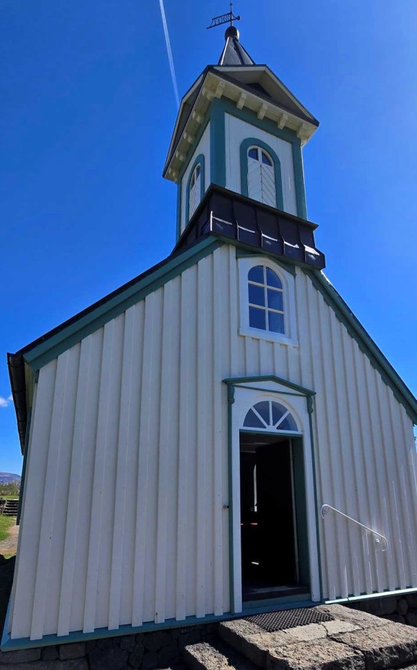 Close-up view of a charming, small church with a pointed roof and bell tower against a clear blue sky.