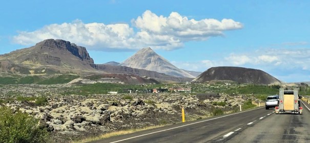 A scenic view of a road with mountains and volcanic land formations in Iceland, with a vehicle driving on the right side.