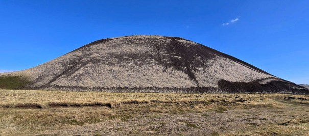 View of Grábrók Crater, showcasing its distinctive conical shape and grassy surroundings under a clear blue sky.