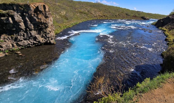 A view of Bruarfoss Waterfall in Iceland, showcasing striking ice blue water flowing through a rocky landscape.