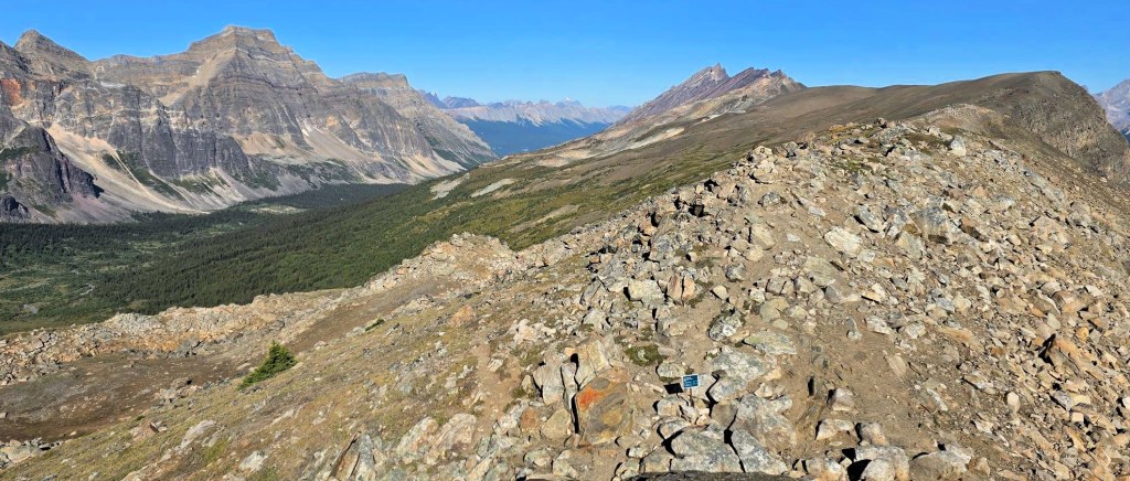 Panoramic view of rocky terrain and steep mountain ridges in a natural landscape, showcasing vibrant blue skies and rocky paths.