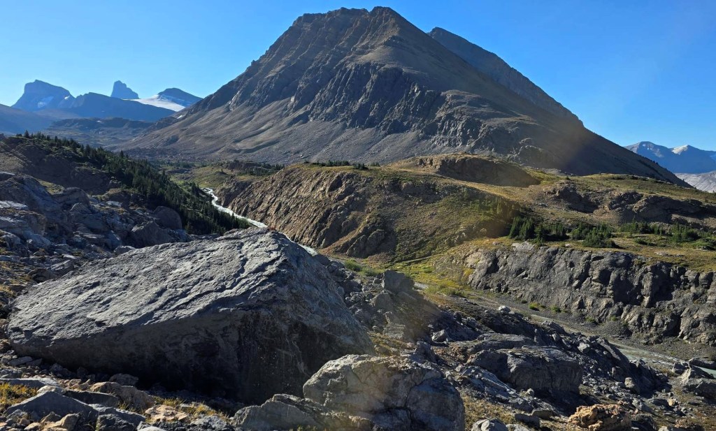 A panoramic view of rugged mountains and valleys in a remote wilderness area, showcasing rocky terrain and sparse vegetation under a clear blue sky.