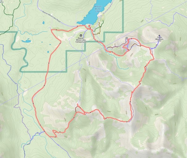 Map showing a hiking trail outlined in red, with features like mountains, lakes, and campgrounds in a forested area.