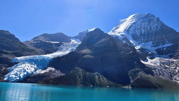 Scenic view of a glacier descending from a mountain peak into a turquoise lake under a clear blue sky.