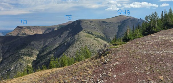 A panoramic view of mountain ridges with labels indicating 'TD,' 'TS,' and '2nd B.' The scene includes a mix of rocky terrain and forested areas under a partly cloudy sky.