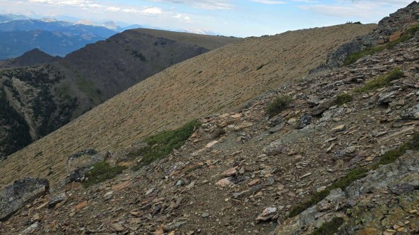 Rocky mountain landscape with a sloped terrain and sparse vegetation under a cloudy sky.