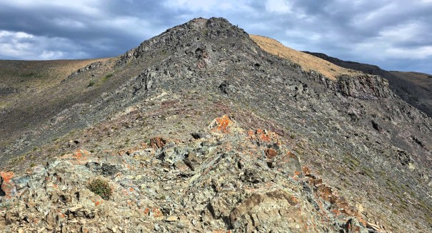 A rugged mountain landscape with rocky terrain and a steep peak under a cloudy sky.