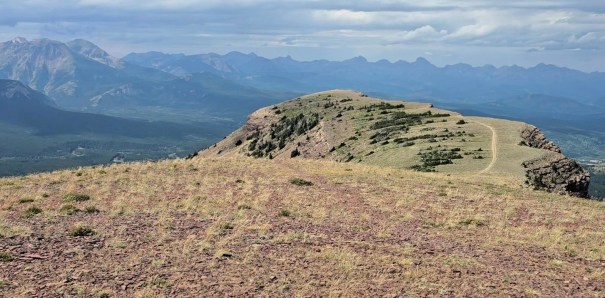 A panoramic view from a rocky hillside overlooking rolling mountains and valleys under a cloudy sky.