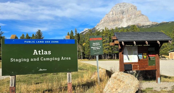 Sign for the Atlas Staging and Camping Area in a public land use zone, with a mountainous backdrop and nearby information kiosk.