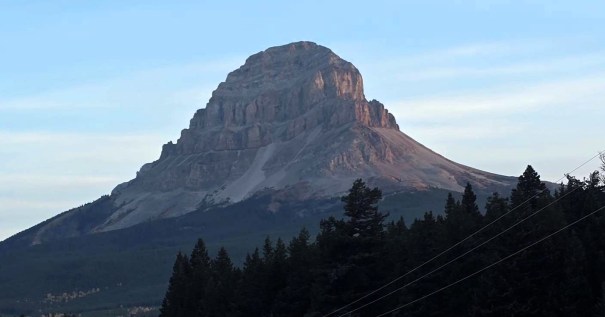 A prominent mountain peak with a flat top, surrounded by trees and a blue sky.