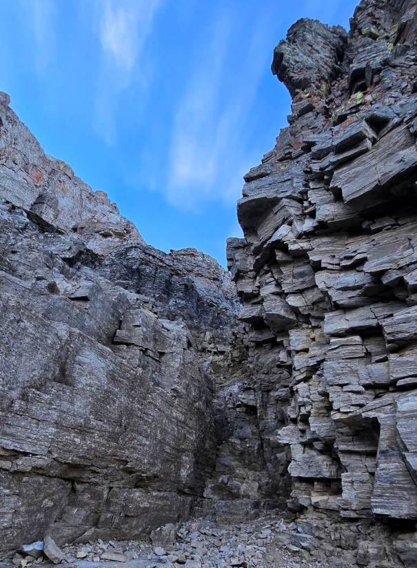 A rocky canyon with steep walls, featuring layered stone formations and a clear blue sky above.