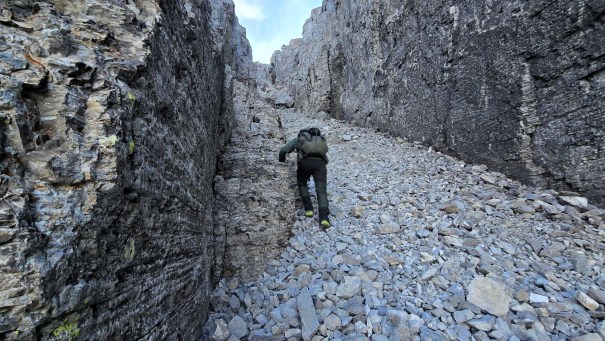 A climber navigating a rocky incline between tall, rough rock formations.