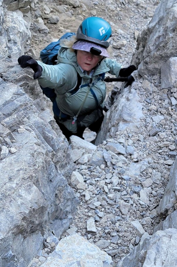 A climber navigating a rocky crevice, wearing a blue helmet and green jacket, focused on climbing.