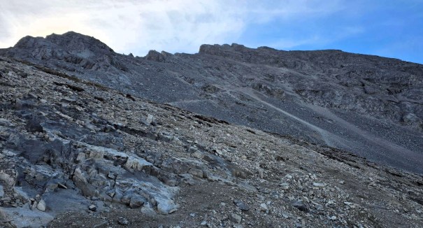 A rocky mountain slope with loose stones and gravel under a blue sky.