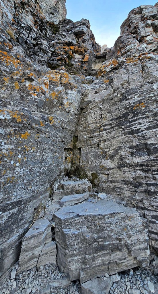 Rocky terrain featuring steep cliffs and rough stone surfaces, with patches of lichen and a small pathway leading upward.